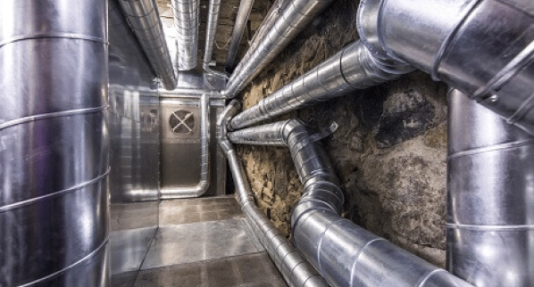 Ductwork installation by mechanical contractors in an industrial underground setting with exposed earth walls and a metal floor.