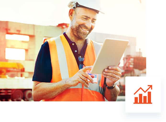Alt text: A happy construction worker using Jonas Construction Software on a tablet, in an outdoor industrial setting.