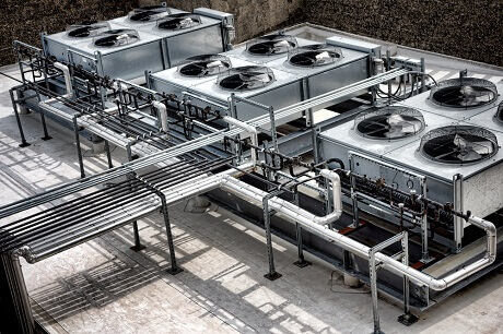 Image of an expansive aerial view showcasing an arrangement of multiple industrial air conditioning units on a building's rooftop. Features include large circular fans and extensive metallic ductwork laid out in a symmetric pattern on a flat concrete surface, signifying the work of specialty contractors in maintenance and service management. This is illustrative of the construction industry Jonas Construction Software caters to.