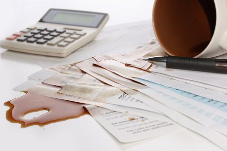 Image showcasing a spilled coffee cup on financial documents related to Jonas Construction Software, with a calculator and pen by its side indicating possible disruption in workflow.