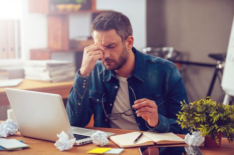 Distressed man at desk with laptop, mechanical contractor project papers, glasses and plant indicating high stress levels in project management in construction.