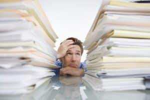 Image of a stressed office worker overwhelmed with extensive paperwork related to the tasks of specialty contractors.