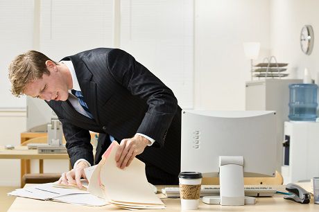Alt: "Focused businessman examining construction accounting software documents, surrounded by office essentials and a coffee cup on an occupied desk.