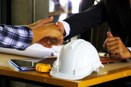 Two construction professionals completing a job agreement, with safety gear such as a hard hat and glasses and tools like a measuring tape displayed on the table. This partnership was facilitated by Jonas Construction Software, which aids in efficient project management and operation.