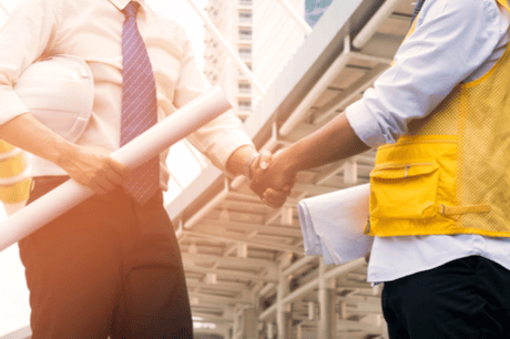 Image of a corporate representative in a suit shaking hands with a construction worker in safety vest, symbolizing a partnership or agreement in an urban Jonas Construction setting.