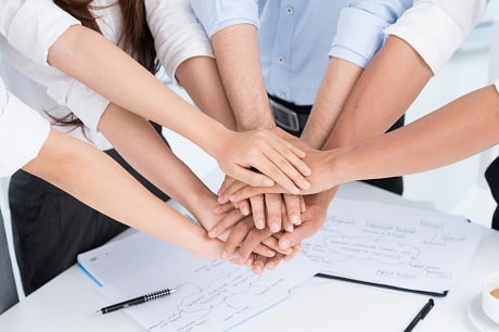 A team of construction professionals forming a united front, with their hands stacked in unity atop a paperwork-laden conference table. This representation of teamwork and collaboration highlights the usage of Jonas Construction's accounting software in managing their projects efficiently.