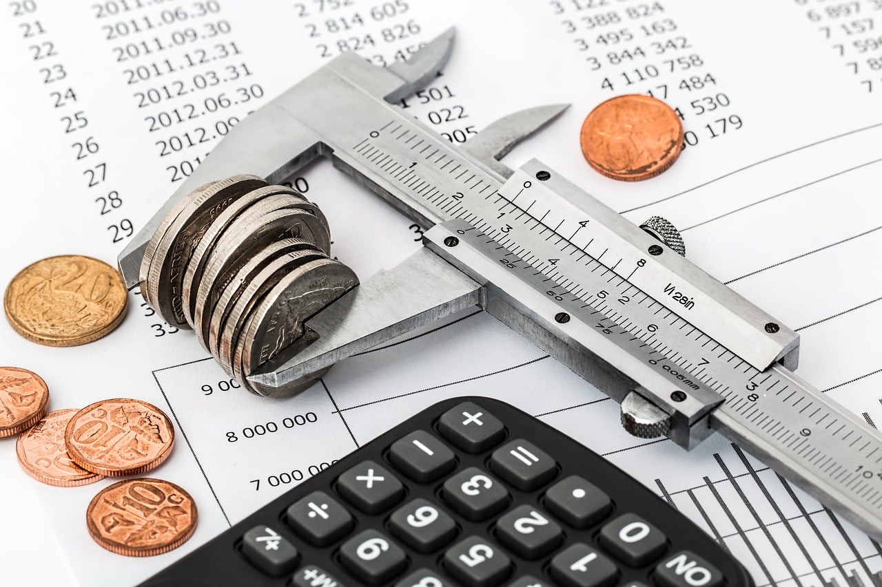 Vernier caliper carefully measuring a stack of coins placed strategically atop financial documents, with a handy calculator and the jumble of extra coins in close vicinity symbolizing the careful internal budgeting and accounting intricacies handled by Jonas Construction Software.