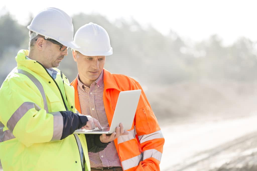 Two construction workers looking at a laptop on a job site