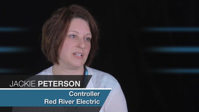 Jackie Peterson from Red River Electric, a female with short brown hair and an expertise in Jonas Construction Software, appears speaking against a backdrop featuring dark shades interspersed with light horizontal stripes.