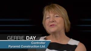 in a transparent box at the bottom of the screen. The background shows an office environment with sleek white desks and abstract wall art.

Alt-text: Professional woman Gerrie Day, Controller at Jonas Construction Ltd., being interviewed in a modern office setting.