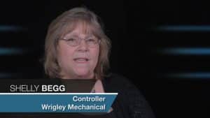 Alt Text: A middle-aged woman named Shelly Begg, controller at Wrigley Mechanical Contractors, with short blond hair and glasses. She is wearing a dark blazer while speaking against a dark background.