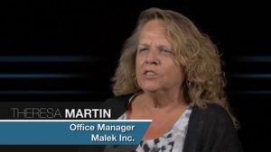 Alt text: "Middle-aged woman with curly blonde hair, identified as Theresa Martin, office manager at Jonas Construction, speaking during an interview on a dark background. A text overlay providing her name and title is present.