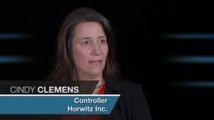 In the image, Cindy Clemens - a controller at Horwitz, is seen engaging in an interview. She is depicted as a professional woman with long brown hair, donned in a black blazer and vibrant red shirt. A graphic overlay introduces her name and position at Horwitz.