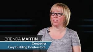 Alt text: Brenda Martin, a short blonde haired woman with glasses and wearing a gray top, identified as the Controller of Jonas Construction, posed against a black background.