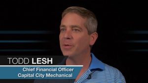 A Chief Financial Officer named Todd Lesh, from Capital City Mechanical Contractors, conducting an interview. Dressed in a striped polo shirt, he is set against a dark background.