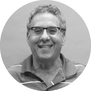 Alt text: Cheerful middle-aged man wearing glasses and a striped polo shirt, representing Jonas Construction against a plain, neutral background.