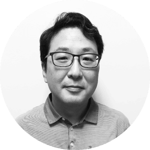 East Asian mechanical contractor portrait with short black hair and glasses, smiling slightly, wearing a collared shirt on a plain background.