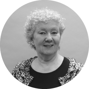 Alt text: Portrait of a friendly elderly woman with short curly hair, smiling softly at the camera. She's sporting a leopard-print blouse and black cardigan, indicative of the poised professionalism ideal for specialty contractors in the construction industry.