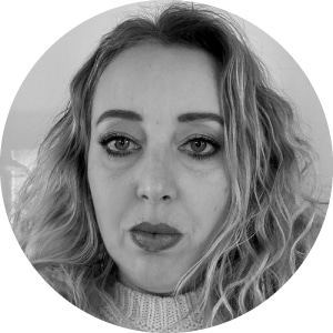 Close-up monochrome portrait of a woman with wavy hair, gazing confidently at the camera; she is clad in a turtleneck sweater and her face is subtly accentuated with eye and lip makeup.