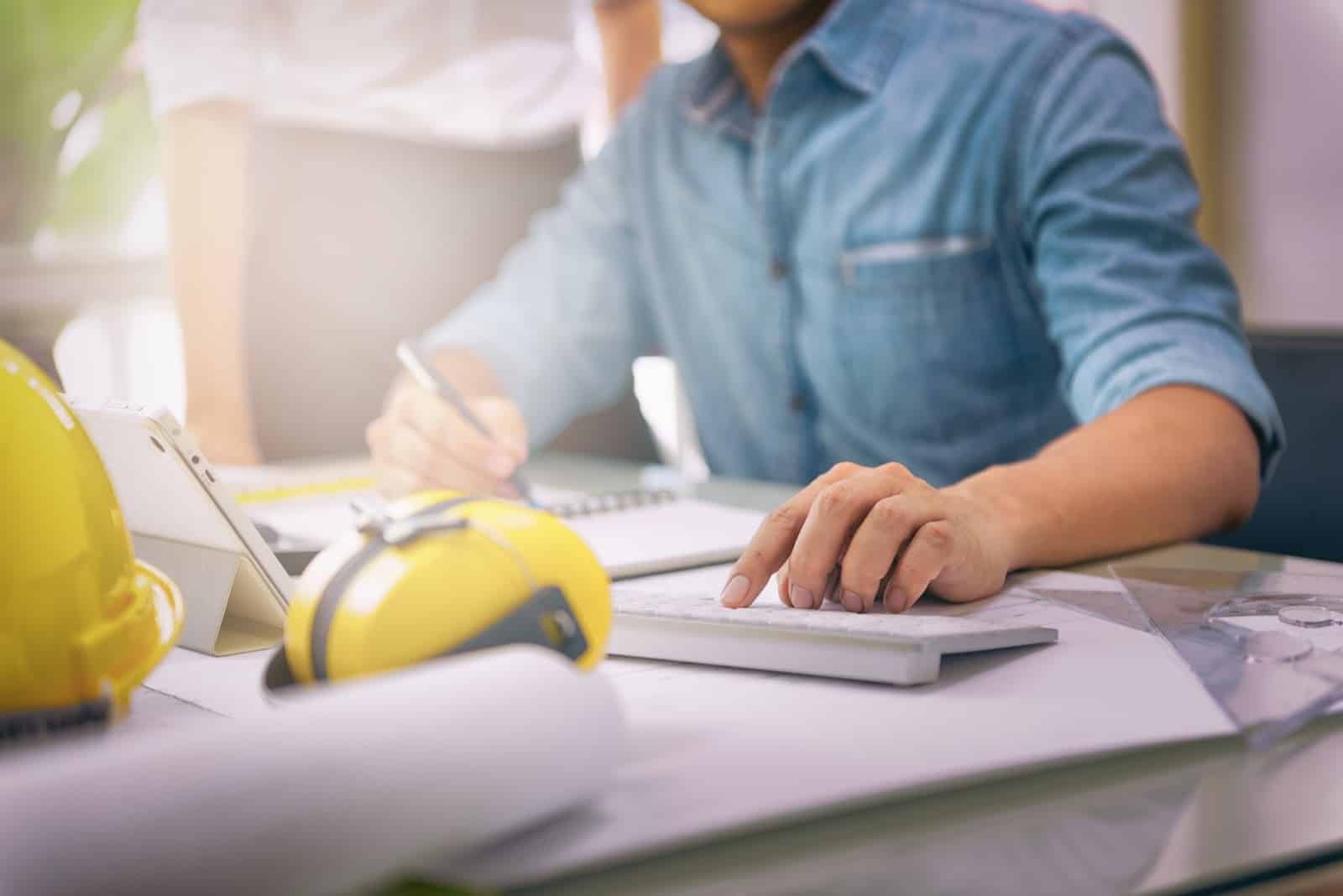 man appears to be in deep concentration as he plans and organizes construction projects. Behind him, a PC screen with Jonas Construction Software interface is visible - highlighting its use in the workflow.