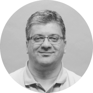 Middle-aged man with glasses smiling slightly, in grayscale, wearing a branded Jonas Construction Software polo shirt.