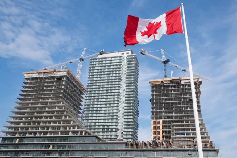 Alt text: Canadian flag waving proudly in a blue sky with two under-construction high-rise buildings in the background, illustrated as being managed by Jonas Construction Software. Building cranes prominently displayed symbolizing progress and growth.