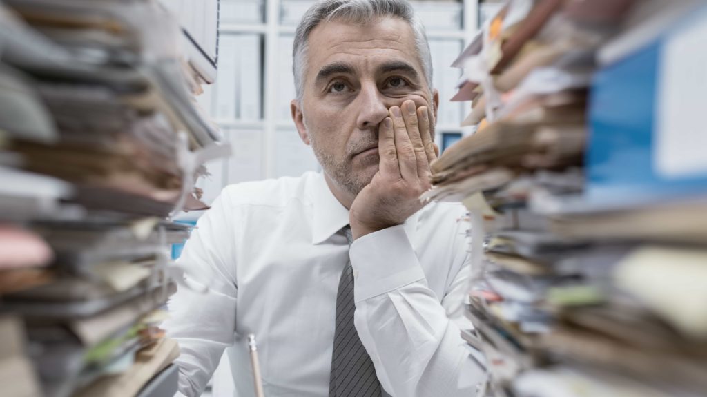 a man looking frustrated with piles of paperwork in front of him