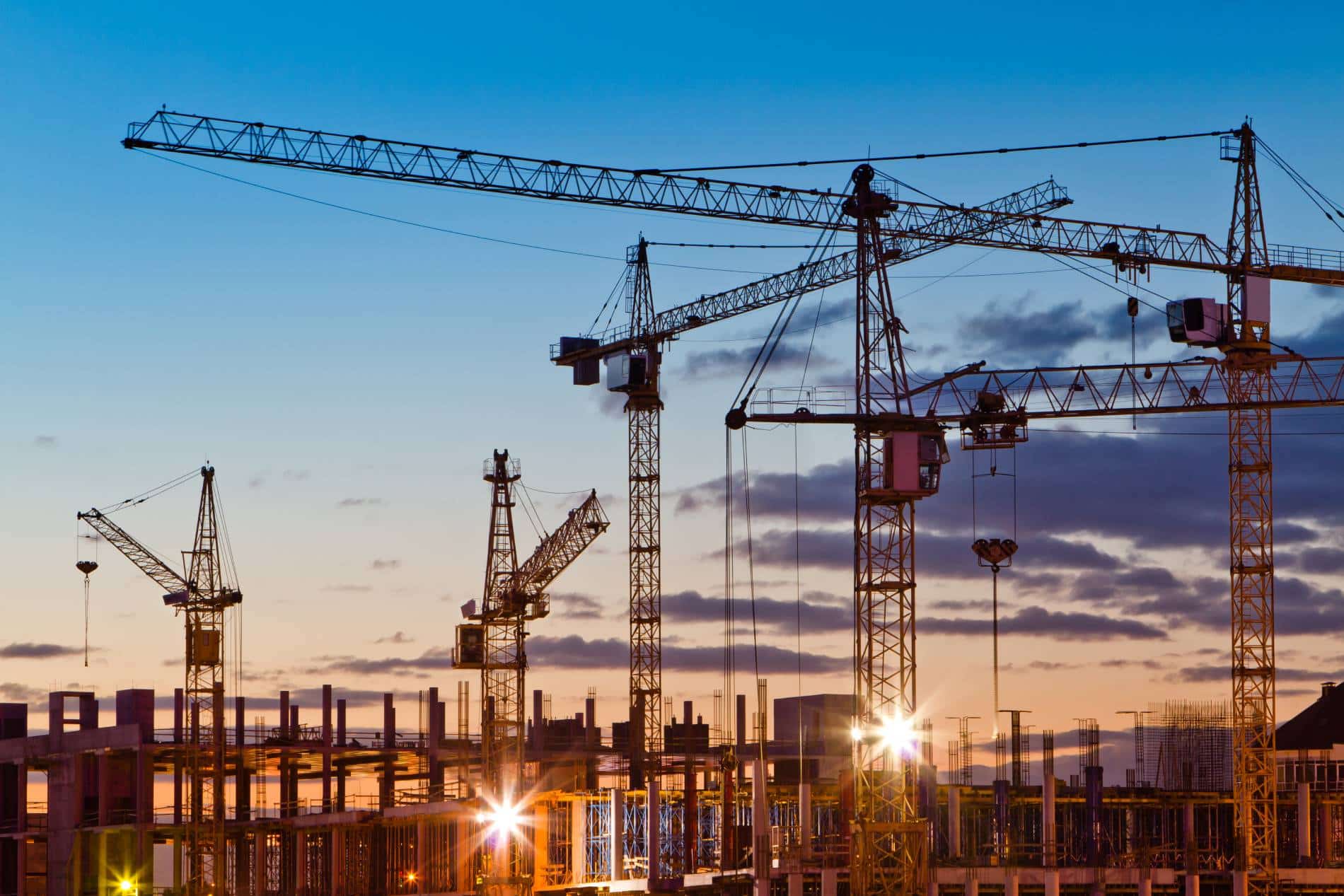 A busy construction site with towering cranes and glowing frameworks, managed by expert contractors at sunset.