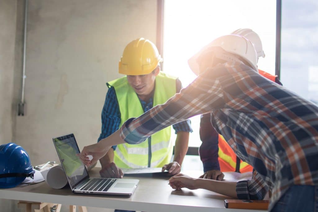 Three construction workers looking at a laptop on a jobsite.