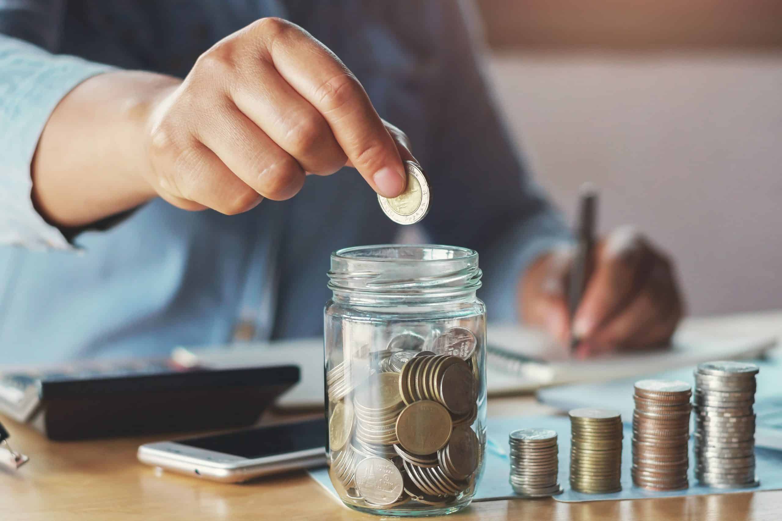 Stacks of coins and a hand putting a coin in a jar full of coins.