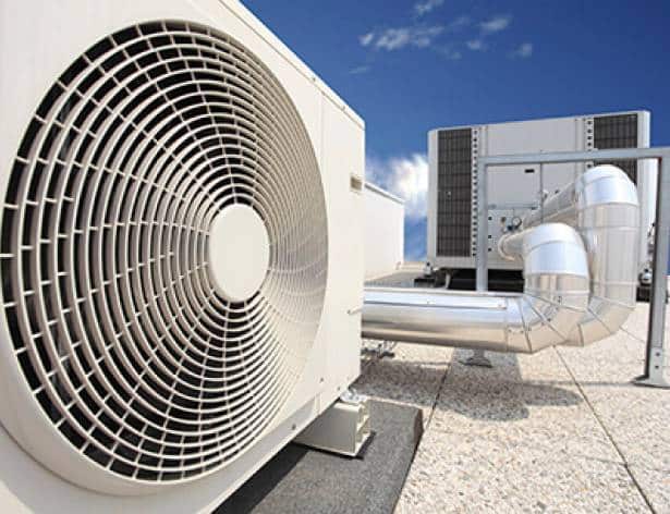 Alt: "White HVAC unit with large fan system sitting on a rooftop under clear blue sky, indicating advanced air conditioning equipment, including additional air handlers and ductwork in the background.