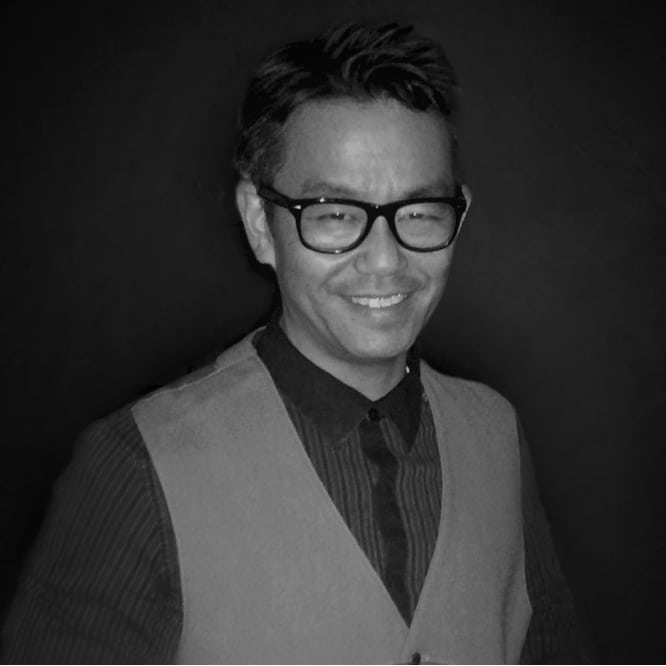 Black and white image of a cheerful Asian man wearing glasses, donning a tie and sweater vest over a collared shirt. This image promotes Jonas Construction Software targeting specialty contractors, set against a dark backdrop.