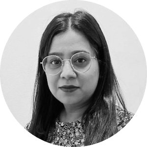 Headshot of a confident and focused woman with medium-length hair, donning round glasses and a patterned top, looking intently at the camera.