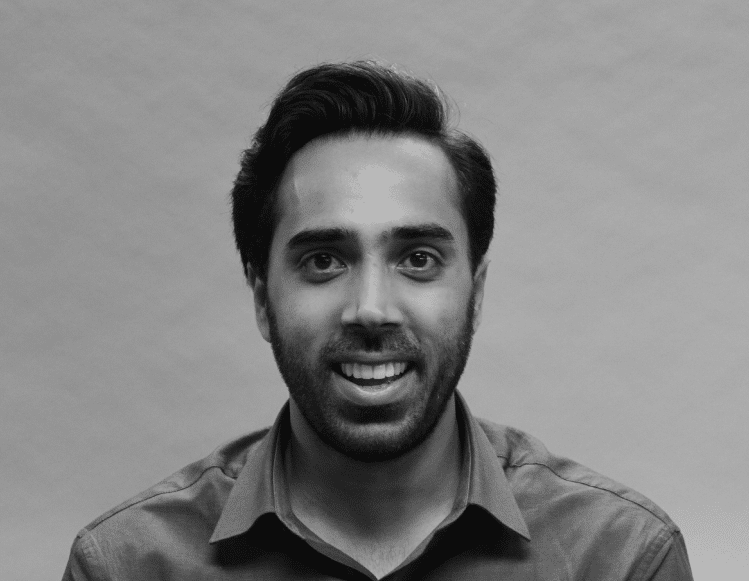 Close-up image of a smiling male mechanical contractor with medium-length dark hair and light beard, wearing a collared shirt against a plain background.